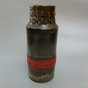 May include: A tall, cylindrical ceramic vase with a dark green glaze and a band of red around the middle. The top of the vase has a row of raised circles with red centers.