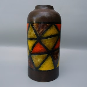May include: A brown ceramic vase with a geometric design. The vase features a cylindrical shape with a narrow neck. The design includes triangles in shades of yellow, orange, and brown, outlined in black.