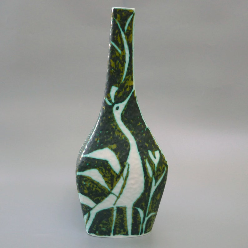 Puede incluir: Un jarr&oacute;n de cer&aacute;mica blanca con un dise&ntilde;o de p&aacute;jaro estilizado en verde y blanco. El jarr&oacute;n tiene un cuello alto y delgado y una base ancha y redondeada.