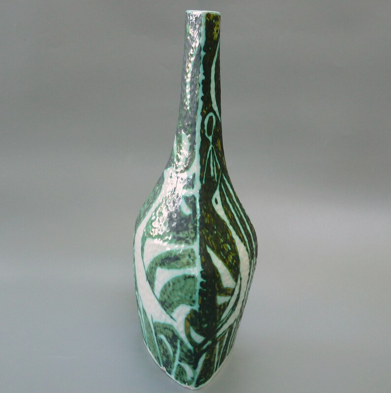 Puede incluir: Un jarr&oacute;n de cer&aacute;mica verde y blanco con un dise&ntilde;o abstracto. El jarr&oacute;n tiene un cuello estrecho y una base ancha y redondeada.