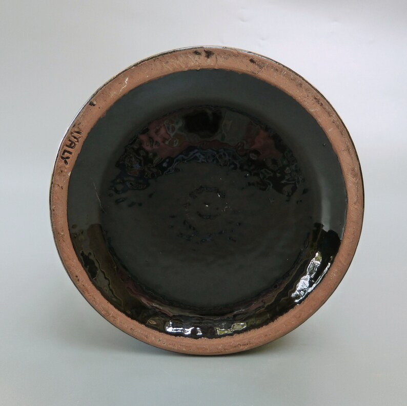 May include: The bottom of a black ceramic vase with a brown rim. The vase has the word "ITALY" stamped on the bottom.