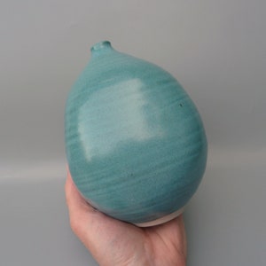 May include: A teal ceramic vase with a rounded, bulbous shape. The vase has a smooth, glossy finish and a slightly uneven, textured surface.