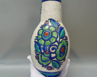May include: A tall, cream-colored ceramic vase with a blue rim and a floral design. The vase features a crackle glaze and a central pattern of green, blue, and red stylized flowers and leaves. The vase is approximately 10 inches tall.