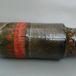 May include: A brown and green ceramic vase with a red band and a textured pattern. The vase has a round, bulbous base and a cylindrical neck.