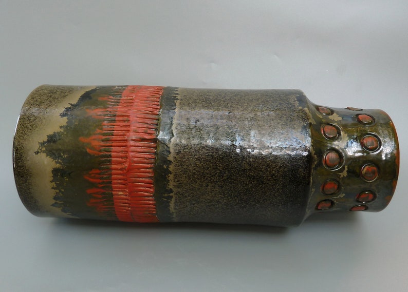 May include: A brown and green ceramic vase with a red band and a textured pattern. The vase has a round, bulbous base and a cylindrical neck.