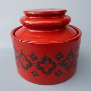 May include: Red ceramic butter dish with a lid. The dish has a black and white geometric pattern around the middle.
