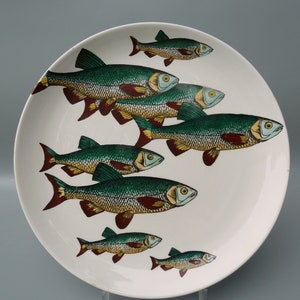 May include: White ceramic plate with a school of fish design. The fish are depicted in shades of green, yellow, and red, swimming across the plate's surface. The plate has a simple, clean design, making it suitable for everyday use or decorative purposes.