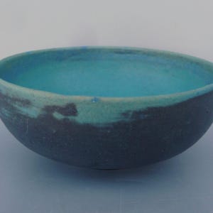 May include: A blue and black ceramic bowl with a textured finish. The bowl is glazed in a light blue color on the inside and a darker blue color on the outside.
