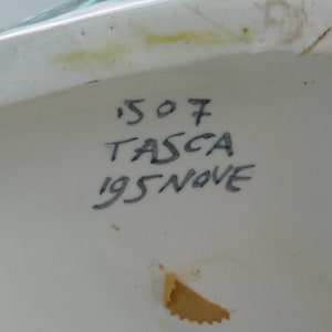 Puede incluir: Primer plano de un objeto de cer&aacute;mica blanca con texto escrito a mano en negro que dice '507 TASCA 195 NOVE'.