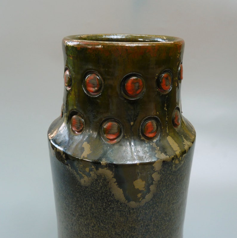 May include: A dark green ceramic vase with a textured surface and a band of raised orange circles around the middle.
