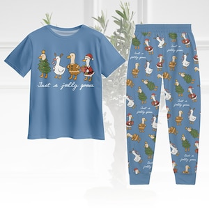 May include: A light blue pajama set featuring a short-sleeved shirt and pants. The shirt has a graphic of geese dressed in Christmas attire with the text "Just a jolly goose." The pants have a repeating pattern of geese, Christmas trees, and text.