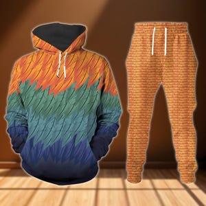 May include: A matching hoodie and tracksuit bottoms set. The hoodie has a feather-like design in orange, green, blue, and black. The tracksuit bottoms have a brick-like pattern in shades of orange. Both items are displayed on a wooden surface.