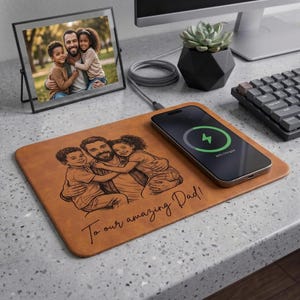 May include: A brown leather desk mat with a family portrait and the text "To our amazing Dad!" A smartphone is charging on the mat. A framed photo of the family is also on the desk.