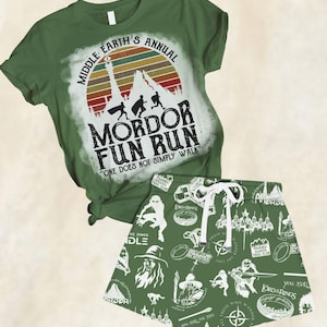 Puede incluir: Conjunto de camiseta y pantalón corto verdes. La camiseta presenta el texto "Middle Earth's Annual Mordor Fun Run" con una silueta de montaña. El pantalón corto tiene un estampado blanco con ilustraciones de El Señor de los Anillos.