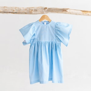 May include: A blue and white gingham dress with puffed sleeves hanging on a wooden hanger.