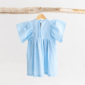 May include: A light blue gingham dress with puffed sleeves and a gathered skirt. The dress is hanging on a wooden hanger.