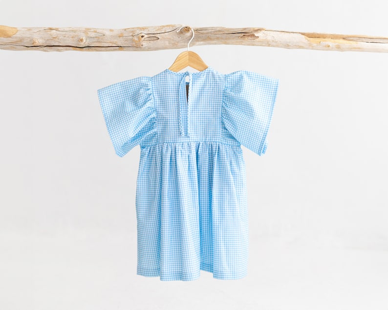 May include: A light blue gingham dress with puffed sleeves and a gathered skirt. The dress is hanging on a wooden hanger.