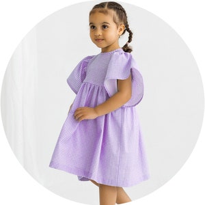 May include: A young girl wearing a purple and white gingham dress with short puffed sleeves. The dress has a gathered skirt and a round neckline.