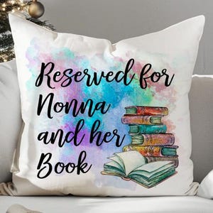 May include: White throw pillow with the text "Reserved for Nonna and her Book" in black script. The pillow features a watercolor design with a stack of books and a colorful background.