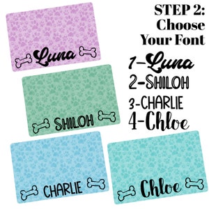 May include: Four personalized dog placemats with paw print designs in pink, green, blue, and green. The placemats feature the names Luna, Shiloh, Charlie, and Chloe in different fonts. The text "STEP 2: Choose Your Font" is displayed above the placemats.