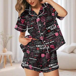 May include: Black pajama set with white trim, featuring a repeating pattern of text, roses, lips, and hearts. The text includes phrases like "Smut Slut", "Wet Panty Book Club", and "Talk Dirty Spicy to Me".