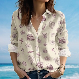 May include: Cream-coloured button-down shirt with a floral and literary print. The design includes flowers, books, feathers, and a typewriter in a muted purple hue. The shirt features the text "You are loved" and "Be kind to your mind".