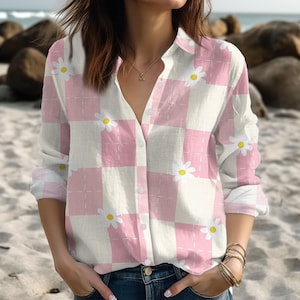 Könnte beinhalten: Ein kariertes Hemd in Rosa und Weiß mit weißen Gänseblümchen. Das langärmlige Hemd hat eine Knopfleiste und ein sich wiederholendes Blumenmuster. Es besteht aus leichtem Stoff und ist ideal für den Frühling.