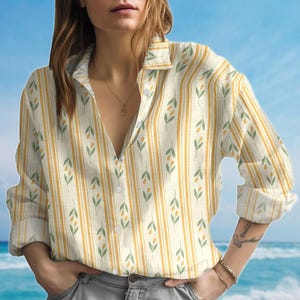 May include: A cream-coloured button-down shirt with vertical yellow stripes. The shirt has a repeating pattern of green leaves and yellow fruit. The sleeves are rolled up, and the top buttons are undone.