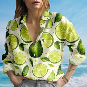 May include: A white button-down shirt adorned with a vibrant lime pattern. The design includes green lime slices, whole limes, and leaves. The shirt has a collared neckline and long sleeves.