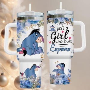 Może przedstawiać: Biały kubek z uchwytem, z niebieskim wzorem z kreskówki Eeyore i napisem "just a Girl who loves Eeyore". Projekt zawiera niebieskie kwiatowe akcenty i słomkę.
