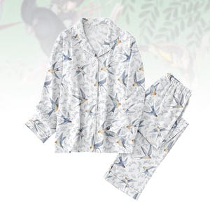 Può includere: Set pigiama bianco con un motivo di uccelli blu e foglie. La parte superiore a maniche lunghe ha una chiusura con bottoni e un colletto a revers. I pantaloni abbinati hanno un elastico in vita. Il set è realizzato in tessuto morbido e leggero.