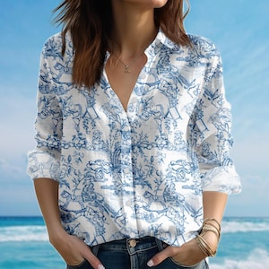 May include: White button-down shirt with a blue toile print depicting figures, trees, and buildings. The long-sleeved shirt has a classic collar and buttoned cuffs. The shirt is made of a lightweight fabric.