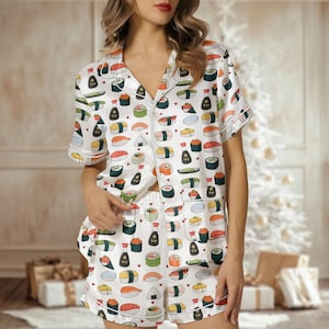 Puede incluir: Conjunto de pijama blanco con estampado de sushi. La parte superior de manga corta y los pantalones cortos presentan varios rollos de sushi, botellas de salsa de soja y pequeños corazones rojos. El conjunto tiene ribetes blancos y una botonadura.