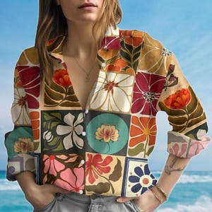 May include: A button-down shirt with a patchwork design featuring floral patterns in shades of orange, red, white, and teal. The shirt has long sleeves and a collared neckline. The background is a blue sky and ocean.