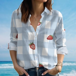 Può includere: Camicia a quadri bianchi e azzurri con maniche lunghe. La camicia presenta un motivo ripetuto di fragole rosse. I bottoni superiori sono aperti.