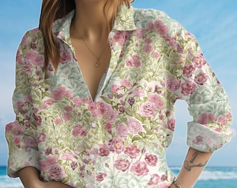 May include: A button-down shirt with a floral pattern featuring pink roses and green leaves on a white background. The shirt has long sleeves and a collared neckline. The background is a blue sky and ocean.