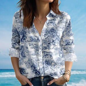 May include: White button-down shirt with a blue toile pattern featuring tigers, elephants, and monkeys in a forest scene. The long-sleeved shirt has a classic collar and is worn with blue jeans.