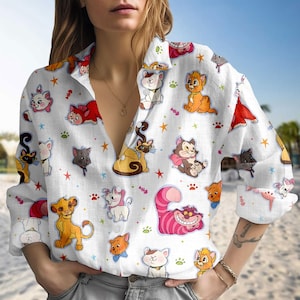 Puede incluir: Camisa blanca con botones con un patrón colorido de gatos de dibujos animados, estrellas y huellas de patas. La camisa de manga larga tiene cuello en V y está hecha de una tela ligera. Las ilustraciones de gatos incluyen varias razas y poses.