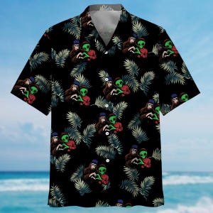 Könnte beinhalten: Ein schwarzes, kurzärmeliges Hemd mit Knöpfen und einem tropischen Druck mit grünen Außerirdischen, die Hüte tragen und mit ihren Händen ein Herz bilden.