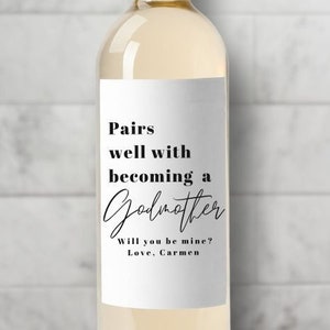 May include: A white wine bottle with a label that says "Pairs well with becoming a Godmother. Will you be mine? Love, Carmen."