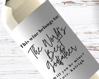 May include: A white wine bottle with a silver label that says "This wine belongs to: The World's Best Godfather. Will you be mine? Love, Kaleigh"