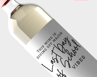 May include: A clear wine bottle with a light pink cap and a white label. The label reads "THIS WINE IS GIVING OFF MAJOR Last Day of School VIBES" in black script. The bottle is filled with a light-colored liquid.