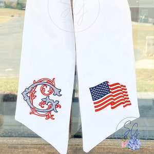 May include: White fabric sash with a red, white, and blue embroidered American flag on one side and a red and blue embroidered letter G with floral embellishments on the other side.