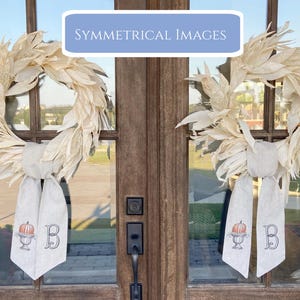 Pu&ograve; includere: Due ghirlande color crema con un design a foglie sono appese a una porta di legno. Ogni ghirlanda ha un fiocco bianco con un'illustrazione di zucca e la lettera "B". Il testo "SYMMETRICAL IMAGES" &egrave; in un rettangolo blu sopra la porta.
