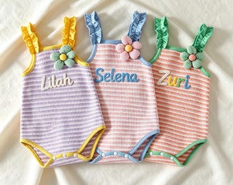 May include: Three baby rompers with names Lilah, Selena, and Zuri embroidered on the front. Each romper has a striped pattern in purple, pink, and orange, with flower accents and ruffled straps. The rompers have yellow, blue, and green trim.
