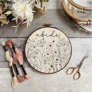 May include: A white embroidery hoop with black embroidery of flowers and the word "abide".