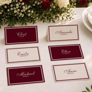 May include: Six rectangular folded place cards featuring a deep burgundy and cream color scheme with a double-line border. The cards display names in elegant script and serif fonts, including Clint Taylor, Amanda Clarkson, Emily Andrews, Elton Clarkson, Michael Philips, and Anne Johnson.