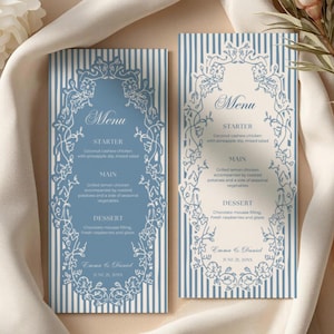 Op de afbeelding: Twee trouwmenukaarten met een blauw-witte gestreepte achtergrond. Elke kaart heeft een decoratief bloemenframe en menudetails. De tekst bevat "Menu", "Voorgerecht", "Hoofdgerecht" en "Dessert".