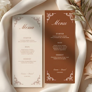 Può includere: Due biglietti del menu di nozze, uno color crema e uno marrone, con una scrittura elegante e decorazioni decorative agli angoli. I menu elencano un pasto di tre portate: antipasto, piatto principale e dessert. I nomi "Emma + Daniel" e una data sono stampati in basso.