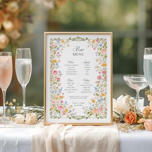 Puede incluir: Un menú de bar enmarcado con un borde dorado y un diseño floral con flores rosas, amarillas y azules. El menú enumera vinos, licores, cerveza y otras bebidas. El texto incluye "Bar Menu" y "Cheers to love, laughter, and happily ever after."
